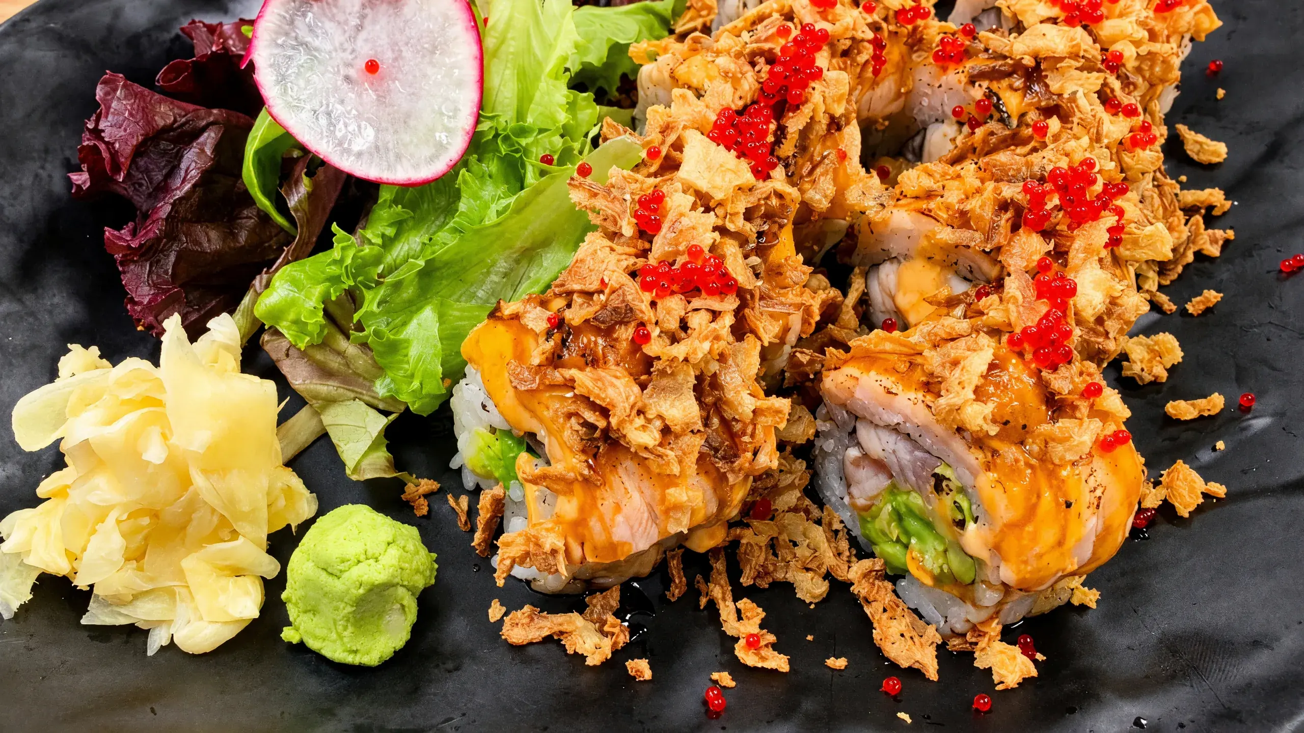 Double Salmon Roll with torched salmon, crispy onion and red tobiko, beside ginger, wasabi and salad